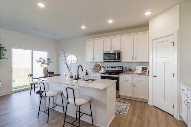 kitchen featuring white cabinets, backsplash, an island with sink, light hardwood / wood-style flooring, and stainless steel appliances