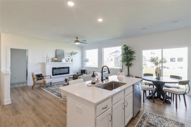 kitchen with sink, dishwasher, light hardwood / wood-style floors, white cabinets, and a kitchen island with sink