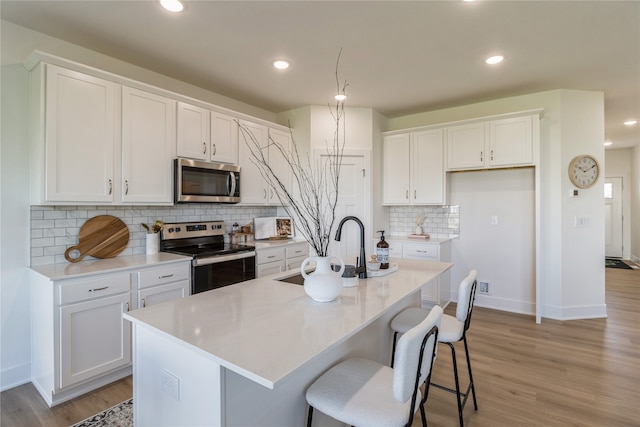 kitchen featuring white cabinetry, stainless steel appliances, light wood-type flooring, and a center island with sink