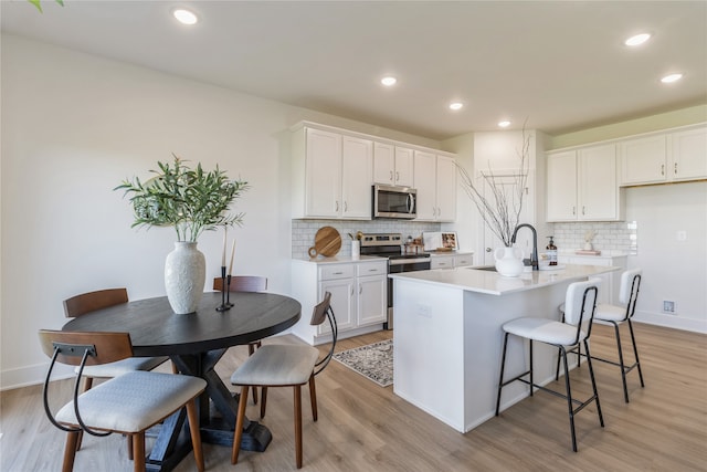 kitchen featuring backsplash, an island with sink, white cabinetry, light wood-type flooring, and stainless steel appliances