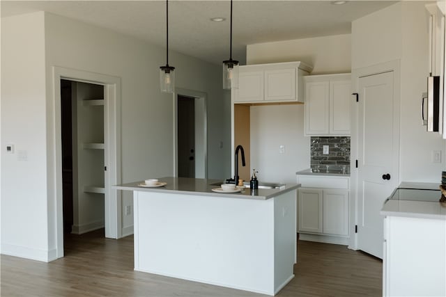 kitchen with decorative light fixtures, sink, an island with sink, white cabinets, and hardwood / wood-style flooring