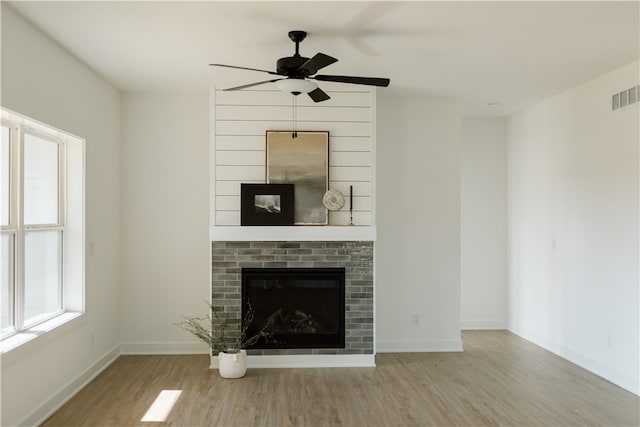 unfurnished living room with a brick fireplace, ceiling fan, and light wood-type flooring