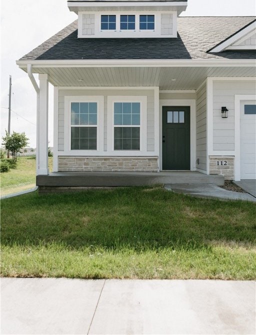 view of exterior entry featuring covered porch, a garage, and a yard