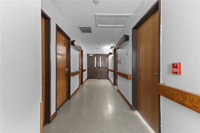 hallway featuring visible vents, baseboards, attic access, and a textured ceiling