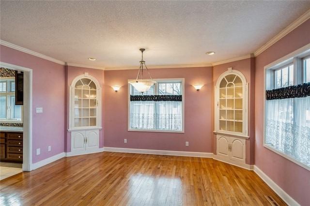 unfurnished dining area featuring crown molding, a wealth of natural light, a textured ceiling, and light wood-type flooring