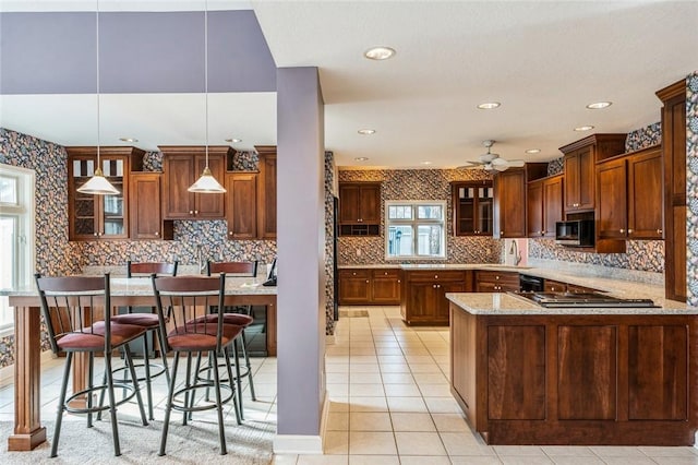 kitchen with tasteful backsplash, a breakfast bar area, hanging light fixtures, light stone counters, and kitchen peninsula