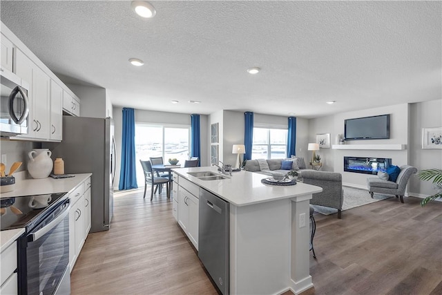 kitchen featuring appliances with stainless steel finishes, a textured ceiling, wood-type flooring, white cabinets, and an island with sink