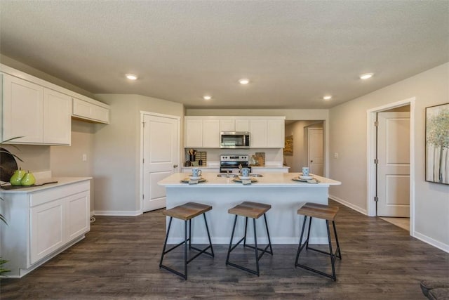 kitchen featuring dark wood-type flooring, a kitchen island with sink, a breakfast bar area, appliances with stainless steel finishes, and white cabinetry