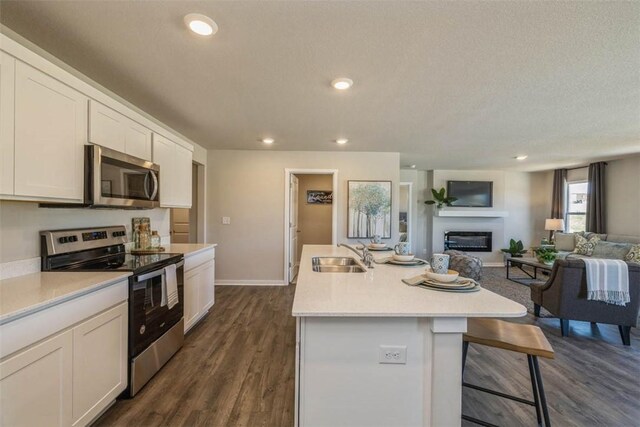 kitchen with appliances with stainless steel finishes, an island with sink, a breakfast bar, white cabinets, and sink