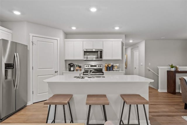 kitchen with a kitchen bar, light wood-type flooring, stainless steel appliances, a center island with sink, and white cabinetry