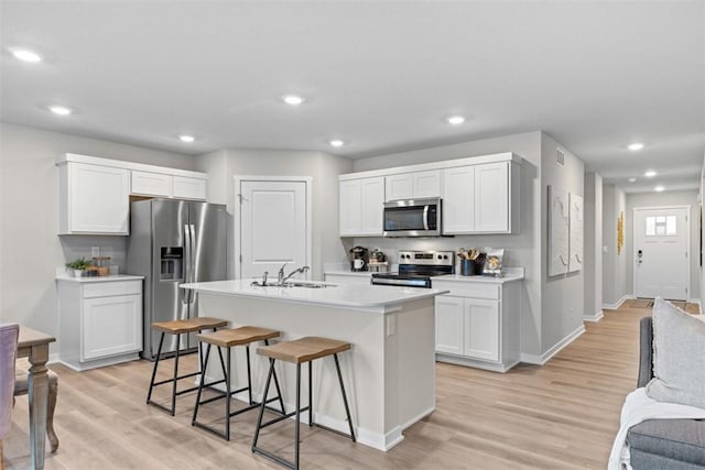 kitchen with white cabinets, light hardwood / wood-style floors, stainless steel appliances, and a kitchen island with sink