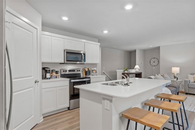 kitchen featuring light wood-type flooring, stainless steel appliances, sink, a center island with sink, and white cabinetry