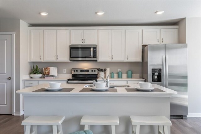 kitchen featuring appliances with stainless steel finishes, white cabinetry, a kitchen bar, light hardwood / wood-style floors, and a center island with sink