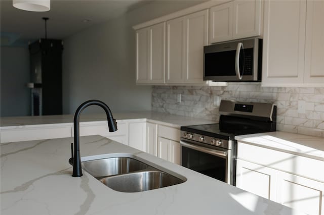 kitchen with sink, tasteful backsplash, light stone counters, white cabinets, and appliances with stainless steel finishes