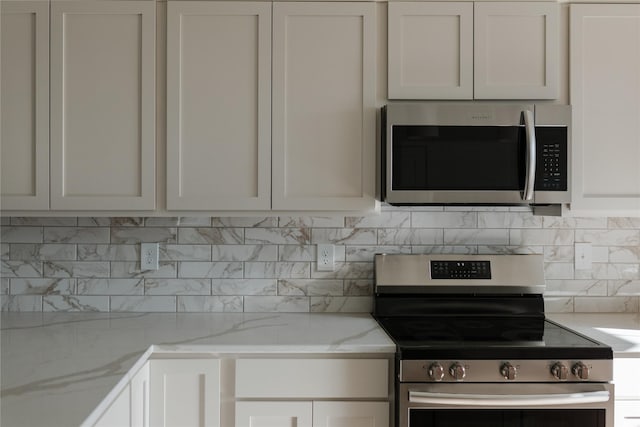 kitchen featuring light stone countertops, appliances with stainless steel finishes, decorative backsplash, and white cabinetry