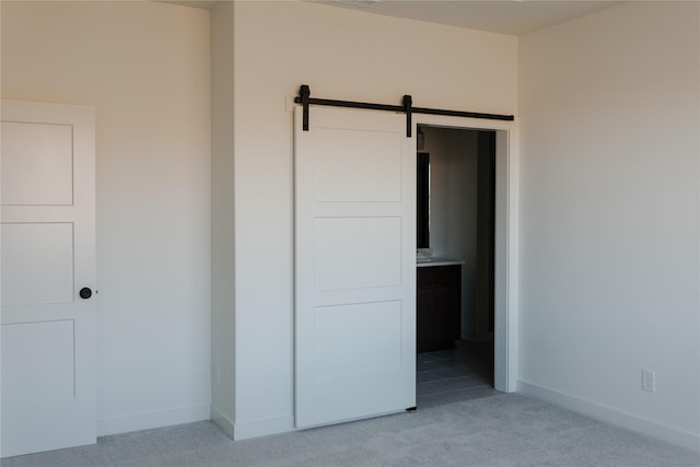 unfurnished bedroom with a barn door, light colored carpet, and ensuite bath