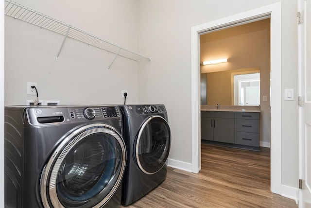 washroom featuring washing machine and dryer, sink, and wood-type flooring