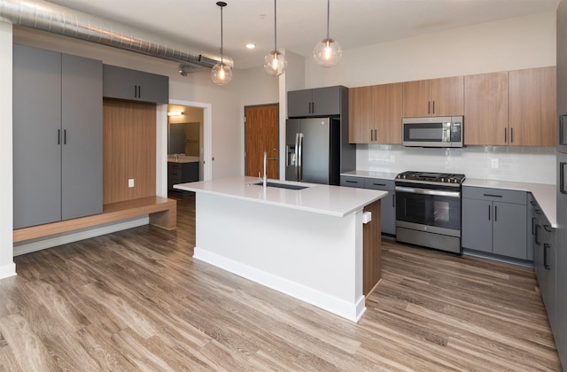 kitchen featuring gray cabinetry, sink, backsplash, a kitchen island with sink, and appliances with stainless steel finishes