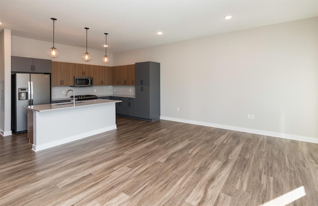 kitchen with a kitchen island with sink, stainless steel appliances, pendant lighting, wood-type flooring, and decorative backsplash