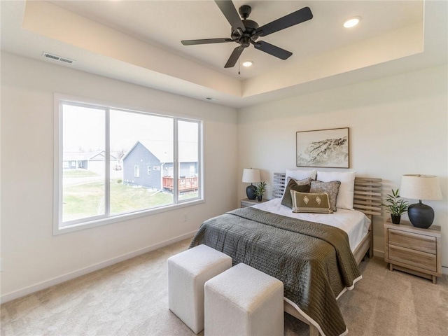 carpeted bedroom with a raised ceiling, multiple windows, and ceiling fan