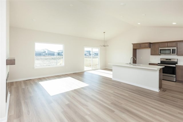 kitchen with decorative light fixtures, stainless steel appliances, light hardwood / wood-style flooring, and an island with sink