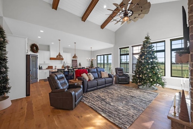 living room with ceiling fan with notable chandelier, beam ceiling, light wood-type flooring, and high vaulted ceiling