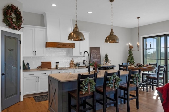 kitchen featuring decorative light fixtures, wood-type flooring, white cabinetry, and an island with sink