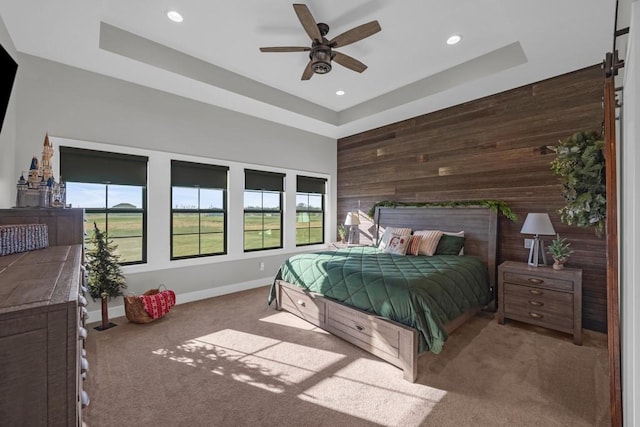 carpeted bedroom featuring a raised ceiling, ceiling fan, and wooden walls