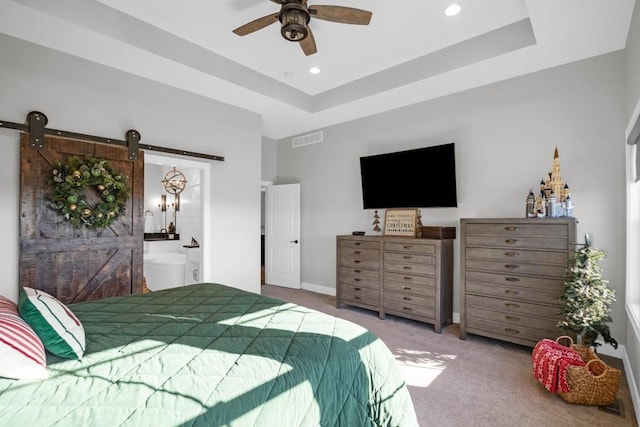 bedroom featuring connected bathroom, a tray ceiling, ceiling fan, a barn door, and carpet floors