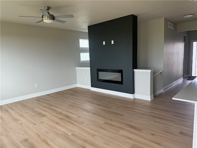 unfurnished living room featuring ceiling fan, a large fireplace, a textured ceiling, and light hardwood / wood-style flooring