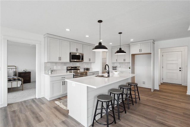 kitchen with hanging light fixtures, sink, decorative backsplash, an island with sink, and appliances with stainless steel finishes