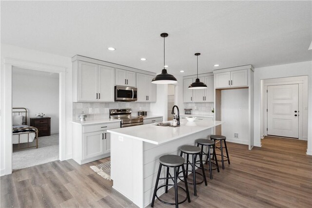 kitchen featuring sink, appliances with stainless steel finishes, hanging light fixtures, an island with sink, and decorative backsplash