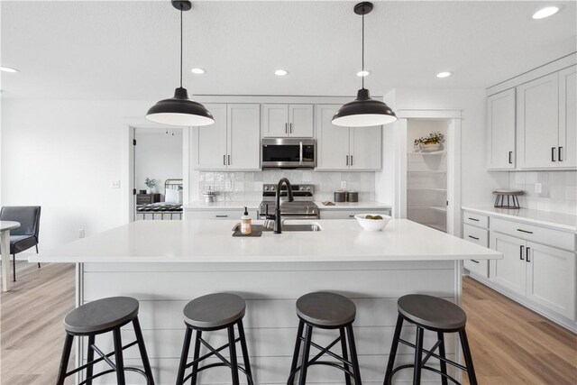 kitchen with sink, hanging light fixtures, an island with sink, decorative backsplash, and appliances with stainless steel finishes