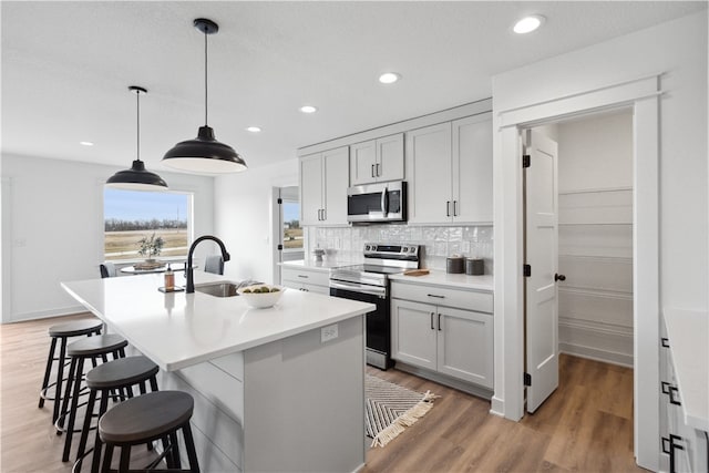 kitchen featuring sink, an island with sink, decorative light fixtures, white cabinetry, and stainless steel appliances