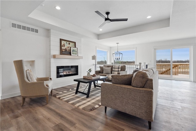 living room with a raised ceiling, ceiling fan, a large fireplace, and hardwood / wood-style flooring