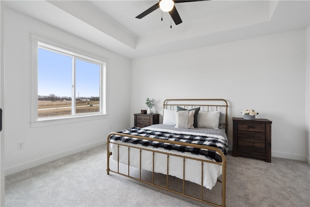 bedroom featuring light carpet, a tray ceiling, and ceiling fan