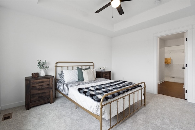 carpeted bedroom with a tray ceiling, ensuite bath, and ceiling fan