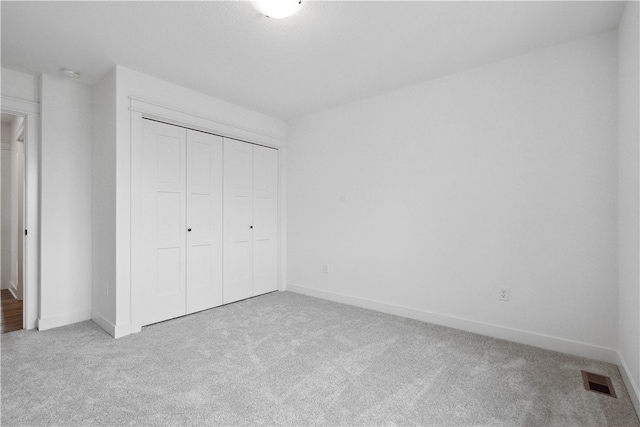 unfurnished bedroom with light colored carpet and a closet