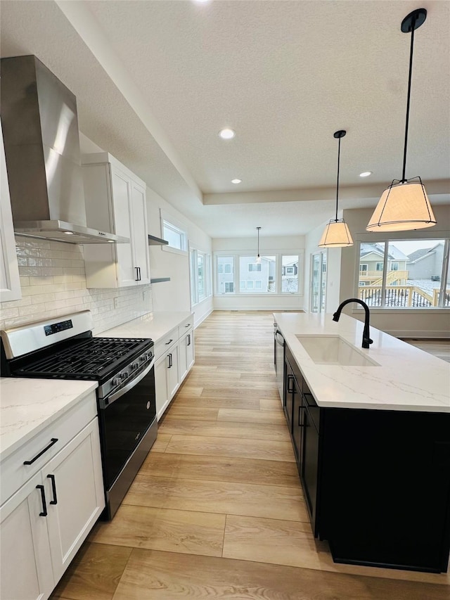 kitchen featuring pendant lighting, appliances with stainless steel finishes, wall chimney exhaust hood, an island with sink, and sink