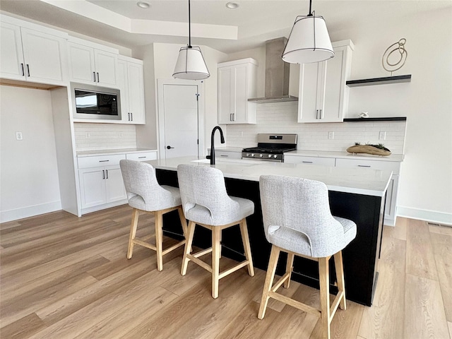 kitchen with white cabinetry, stainless steel gas range, a kitchen island with sink, and wall chimney exhaust hood