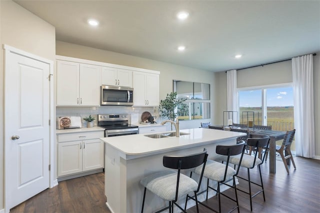 kitchen with a kitchen island with sink, white cabinetry, dark hardwood / wood-style floors, appliances with stainless steel finishes, and sink