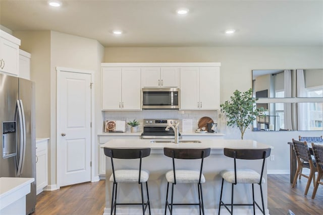 kitchen with dark wood-type flooring, backsplash, appliances with stainless steel finishes, a kitchen bar, and a center island with sink