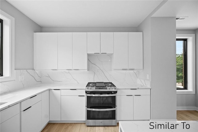 kitchen with white cabinetry, backsplash, double oven range, light stone counters, and light hardwood / wood-style flooring