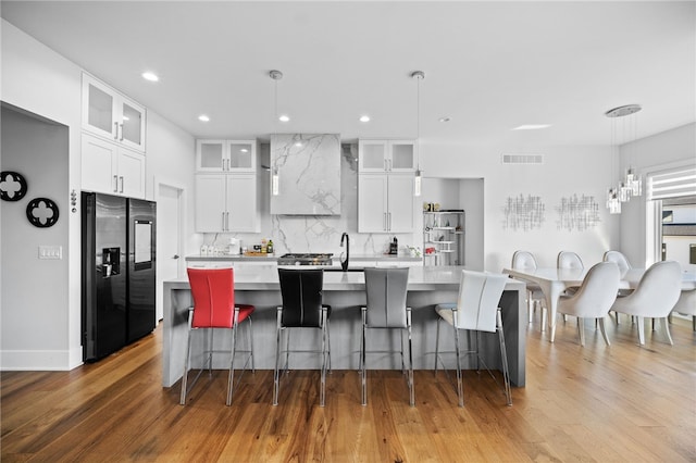 kitchen with white cabinets, black fridge with ice dispenser, wood-type flooring, and an island with sink