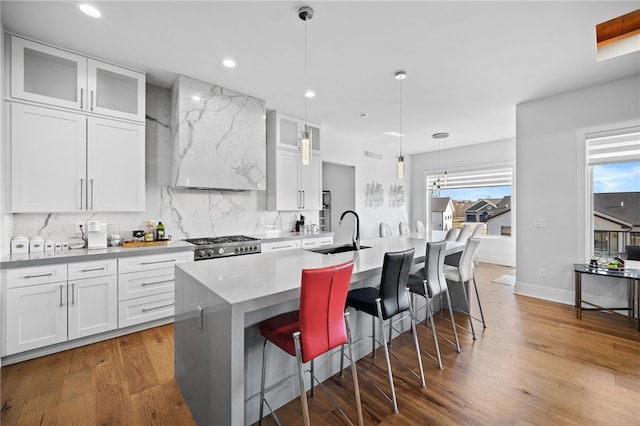 kitchen featuring sink, pendant lighting, wood-type flooring, a center island with sink, and white cabinets