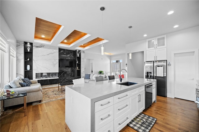 kitchen featuring dishwasher, sink, stainless steel fridge, an island with sink, and white cabinets