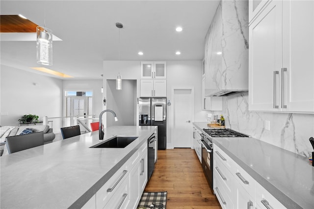 kitchen with stainless steel appliances, sink, decorative light fixtures, light hardwood / wood-style flooring, and white cabinetry