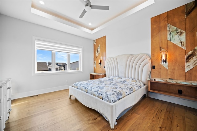 bedroom with ceiling fan, a raised ceiling, and light hardwood / wood-style flooring