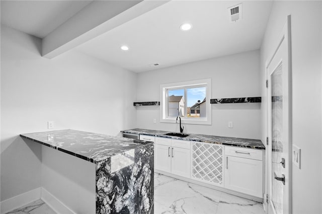 kitchen with kitchen peninsula, white cabinetry, dark stone counters, and sink