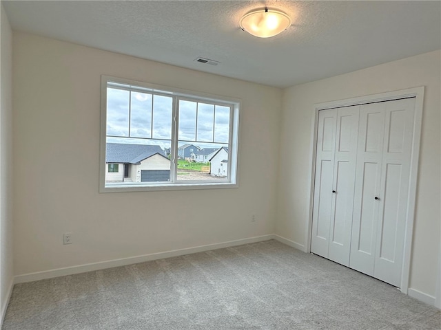 unfurnished bedroom featuring light carpet, a closet, and a textured ceiling